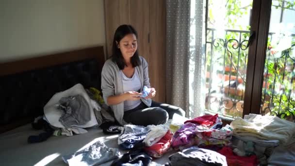 Mom Stacks Clean Baby Clothes Piles While Sitting Bed Next — Wideo stockowe