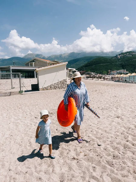 Grandmother with a little girl walk along the sandy beach in hats. High quality photo