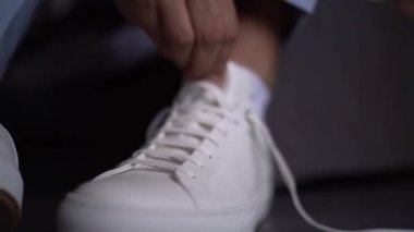 Groom puts on white leather sneakers and adjusts his heels. High quality FullHD footage