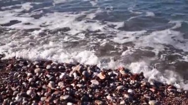 Sea waves with white foam roll on a multi-colored pebble beach. Close-up. High quality FullHD footage