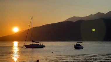 Anchored yachts sway on the waves against the backdrop of mountains at sunset. High quality 4k footage
