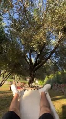 Male legs in sneakers on a hammock swinging under a tree. High quality 4k footage