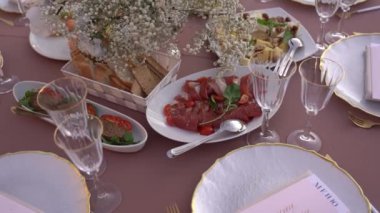 Dishes with cold cuts of meat and vegetables stand on a set table next to plates with signs. High quality FullHD footage