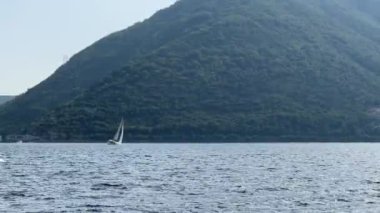 Motorboat and sailboat float on the sea along the green mountains. High quality 4k footage