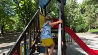 Little girl climbs the stairs and slides down the slide on the playground. High quality 4k footage