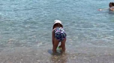 Little girl washing a plastic shovel in the sea. High quality 4k footage