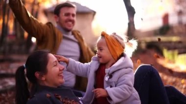 Dad throws handfuls of yellow leaves over sitting mom and daughter. High quality 4k footage