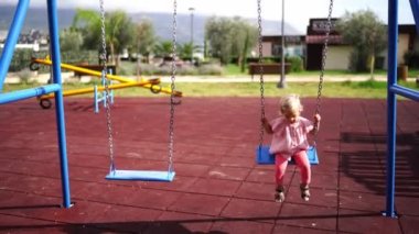 Little girl jumps off the chain swing and runs across the playground. High quality 4k footage