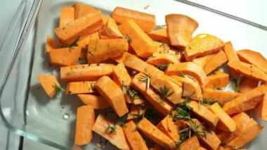 Sliced sweet potato with rosemary and spices lies on a glass dish. High quality 4k footage