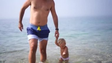 Dad and little girl come out of the sea holding hands and stepping carefully. High quality 4k footage