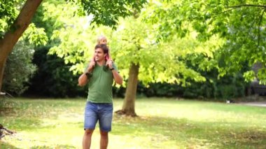 Dad with a little girl on his shoulders walks through a green park among the trees. High quality 4k footage