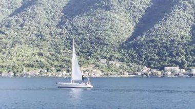 Sailing yacht sails along the sea along a mountainous coast. Montenegro. High quality 4k footage