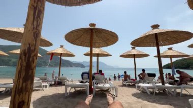 People relaxing on the beach near the sea under straw umbrellas. High quality 4k footage