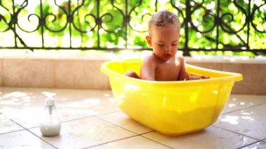 Little girl with wet hair sits in a bowl of water and plays. High quality 4k footage