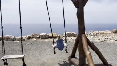 Little girl swings on a wooden swing on a mountain above the sea. Back view. High quality 4k footage