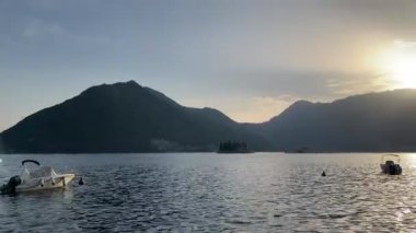 Boats moored off the coast of Perast sway on the waves against the backdrop of mountains and islands. Montenegro. High quality 4k footage