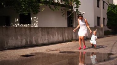 Little girl with her mom in flip-flops runs through the puddles, splashing. High quality 4k footage