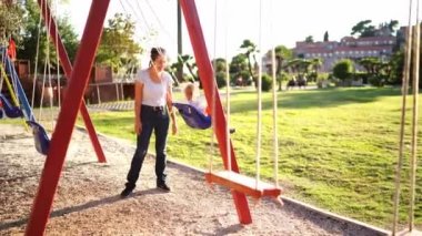 Mom pushes a rope swing with a little girl on the playground. High quality 4k footage