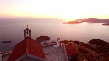 Gelin ve damat, Sveti Stefan adasına tepeden bakan St. Sava Kilisesi 'nin gözlem güvertesinde duruyor. Yüksek kalite 4k görüntü