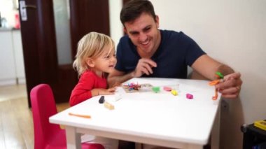 Dad shows a plasticine man to a smiling girl sitting at the table. High quality 4k footage