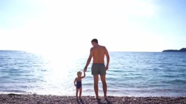 Dad with a little girl stand on the seashore by the sea, holding hands. High quality 4k footage
