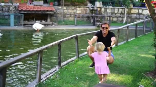 Маленька Дівчинка Біжить Свого Батька Який Присідає Біля Паркану Ставка — стокове відео
