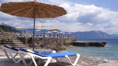 Straw sun umbrella stands near two sun loungers on a sandy beach. High quality 4k footage