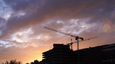 Crane works at a construction site against the backdrop of the sunset sky. High quality 4k footage