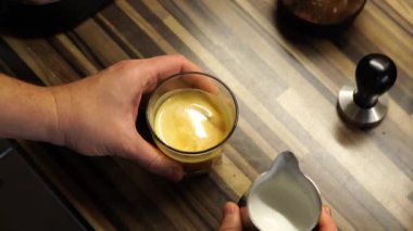 Barista adds milk to a glass of coffee while stirring it. High quality 4k footage