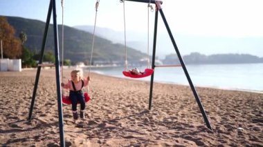 Little girl swings on a swing on a sandy beach by the sea. High quality 4k footage