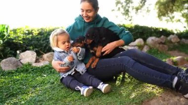 Küçük köpek yavruları çimenlerde oturan anne ve küçük kızın yüzünü yalıyor. Yüksek kalite 4k görüntü