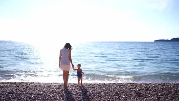 ママは海にビーチに沿って水着の女の子をリードしています バックビュー 高品質4K映像 — ストック動画