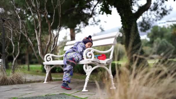 Маленький Ребенок Комбинезоне Забирается Деревянную Скамейку Парке Высококачественные Кадры — стоковое видео