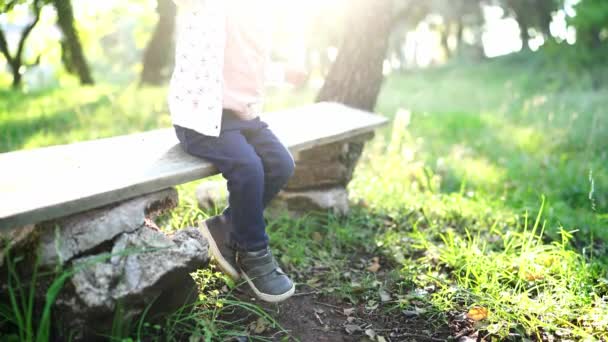 Маленький Ребенок Сидит Скамейке Солнечном Парке Качает Ногами Высококачественные Кадры — стоковое видео