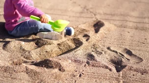 Bambina Siede Sulla Spiaggia Versa Sabbia Con Una Pala Giocattolo — Video Stock