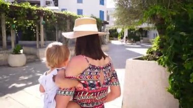 Mom with a child in her arms walks along the road to the pergola near the house. High quality FullHD footage