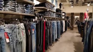 Shelves with folded jeans and hangers with hanging pants in a store. High quality FullHD footage