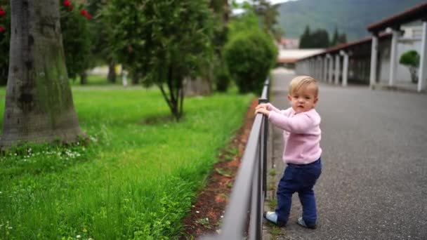 Little Girl Stands Next Fence Park Crouches High Quality Footage — Stockvideo