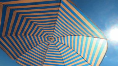 Sun umbrella in blue and yellow stripes against the sunny sky. High quality 4k footage