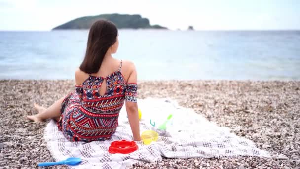 Mujer Joven Sienta Una Manta Una Playa Guijarros Mira Mar — Vídeos de Stock