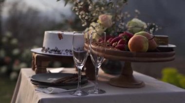Glasses, a wedding cake and fruit in a vase stand on a laid table. High quality FullHD footage