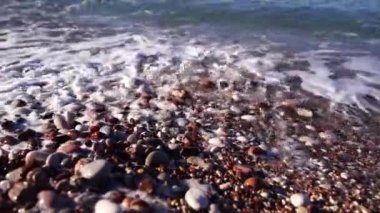 Sea waves with white foam cover multi-colored pebbles. Close-up. High quality FullHD footage