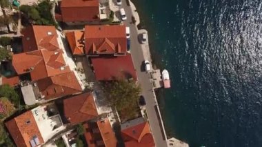 Red roofs of Perast houses near the road on the seashore. Drone. High quality 4k footage