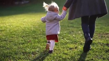Little girl with her mother in coats run along the green lawn, holding hands. High quality FullHD footage