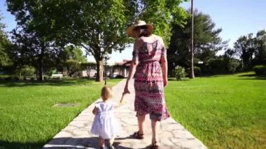 Annem ve küçük bir kız el ele tutuşarak parkta yürüyorlar. Arkadan bak. Yüksek kaliteli FullHD görüntüler