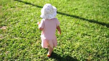 Little girl learns to walk on a green lawn by balancing her arms. High quality FullHD footage