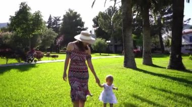 Mom walks holding hands with a little girl through a green park. High quality FullHD footage