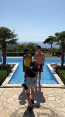 Girl photographer photographs a man and a woman standing on the edge of the pool. High quality 4k footage