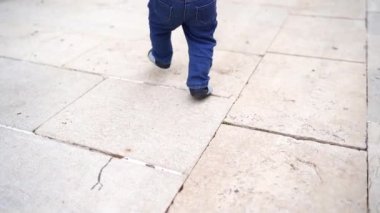 Small baby walks on tiles in tiny shoes. Back view. Cropped. High quality FullHD footage