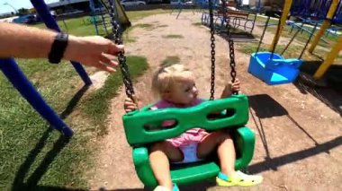 Dad swings a little girl on a chain swing on a playground near an apartment building. High quality FullHD footage
